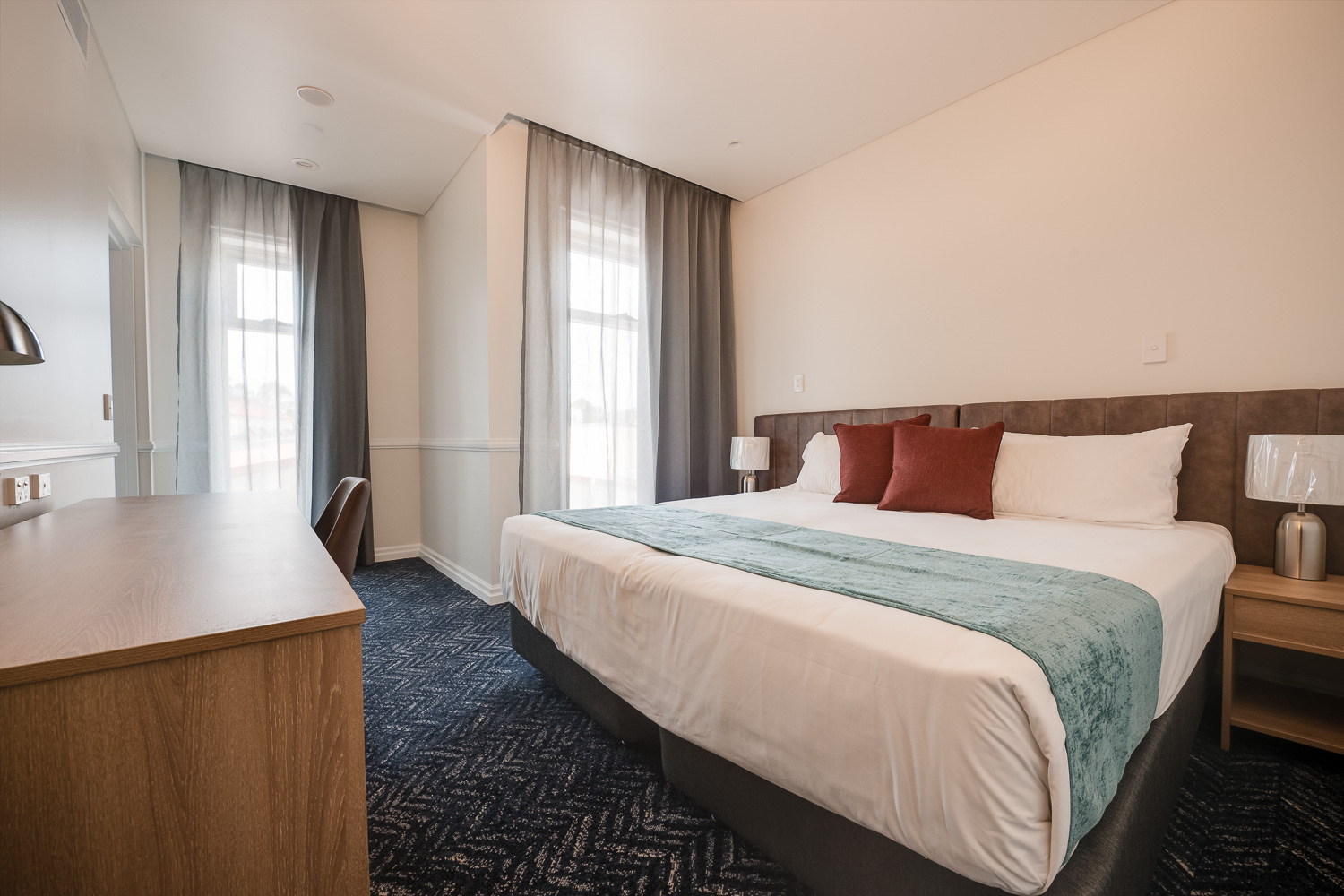 King bed with bedside tables and window in a Logan Village Hotel suite